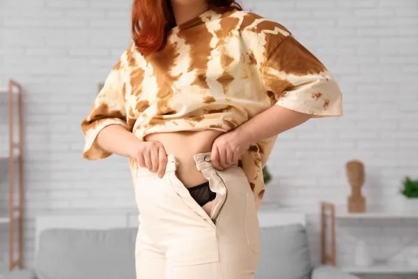 Image of woman trying to do her trousers up after pregnancy weight gain Romford